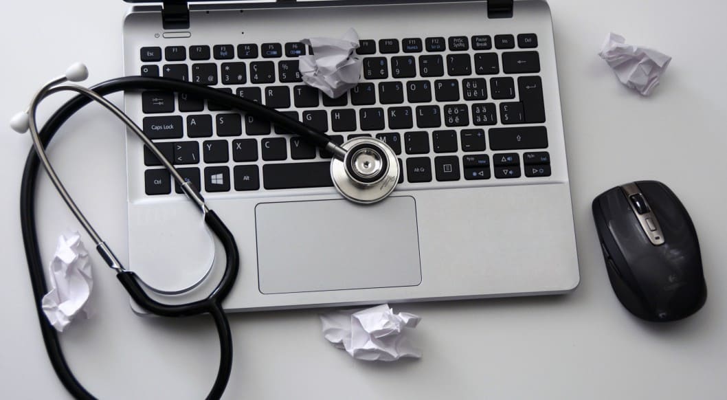 Laptop mit Stethoskop Ein Laptop mit Stethoskop und zerknülltem Papier